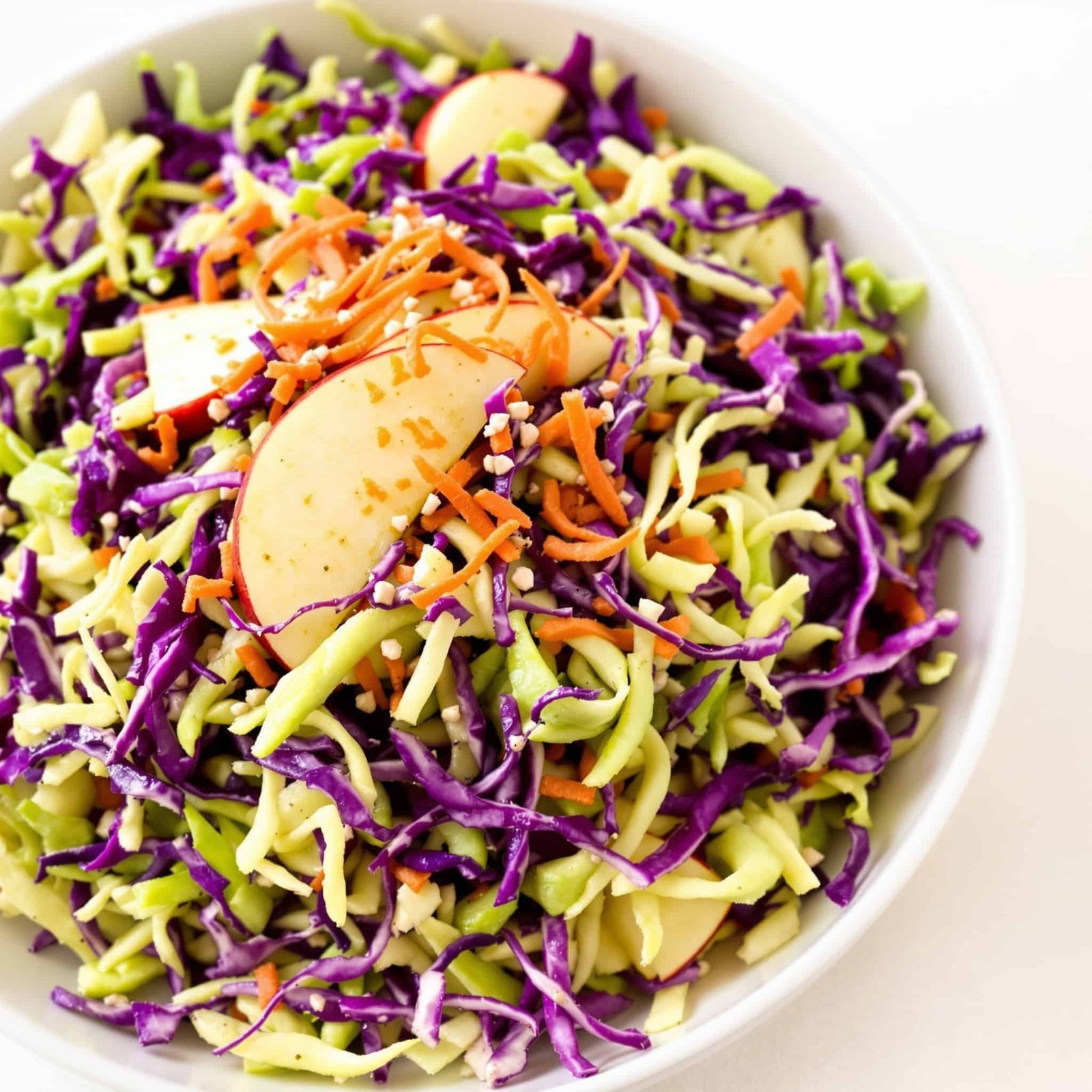Crunchy Apple and Cabbage Slaw Recipe Crunchy apple and cabbage slaw in a bowl, garnished with apples and carrots, showcasing vibrant colors.